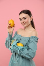 Woman with string bag of fresh lemons on pink background