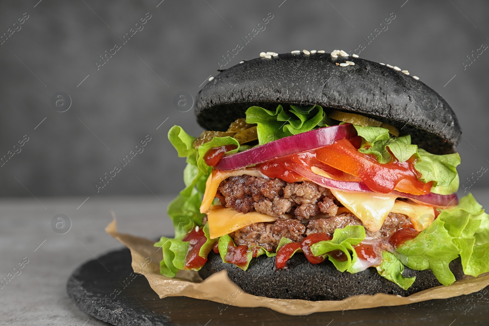 Photo of Slate plate with black burger on table, closeup. Space for text