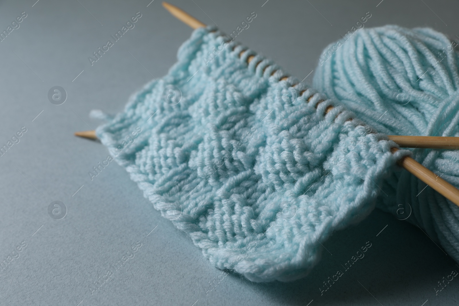 Photo of Soft turquoise knitting and needles on light blue background, closeup