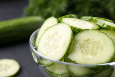 Photo of Cut cucumber in glass bowl on dark gray table, closeup