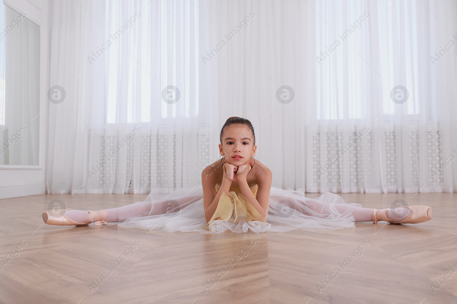 Photo of Beautifully dressed little ballerina sitting on split in studio. Space for text