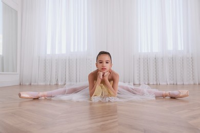 Beautifully dressed little ballerina sitting on split in studio. Space for text