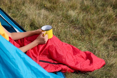 Photo of Woman with cup of drink in sleeping bag outdoors, closeup. Space for text