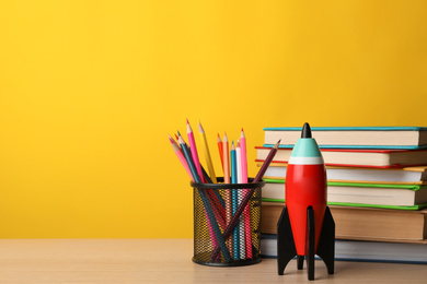 Photo of Bright toy rocket and school supplies on wooden table. Space for text