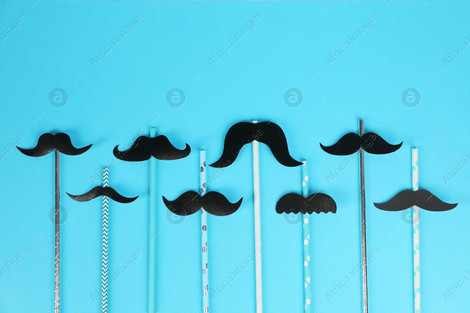 Photo of Fake paper mustaches with party props on light blue background, flat lay. Space for text