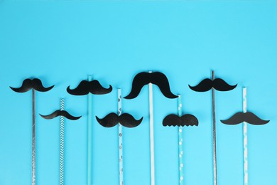 Photo of Fake paper mustaches with party props on light blue background, flat lay. Space for text