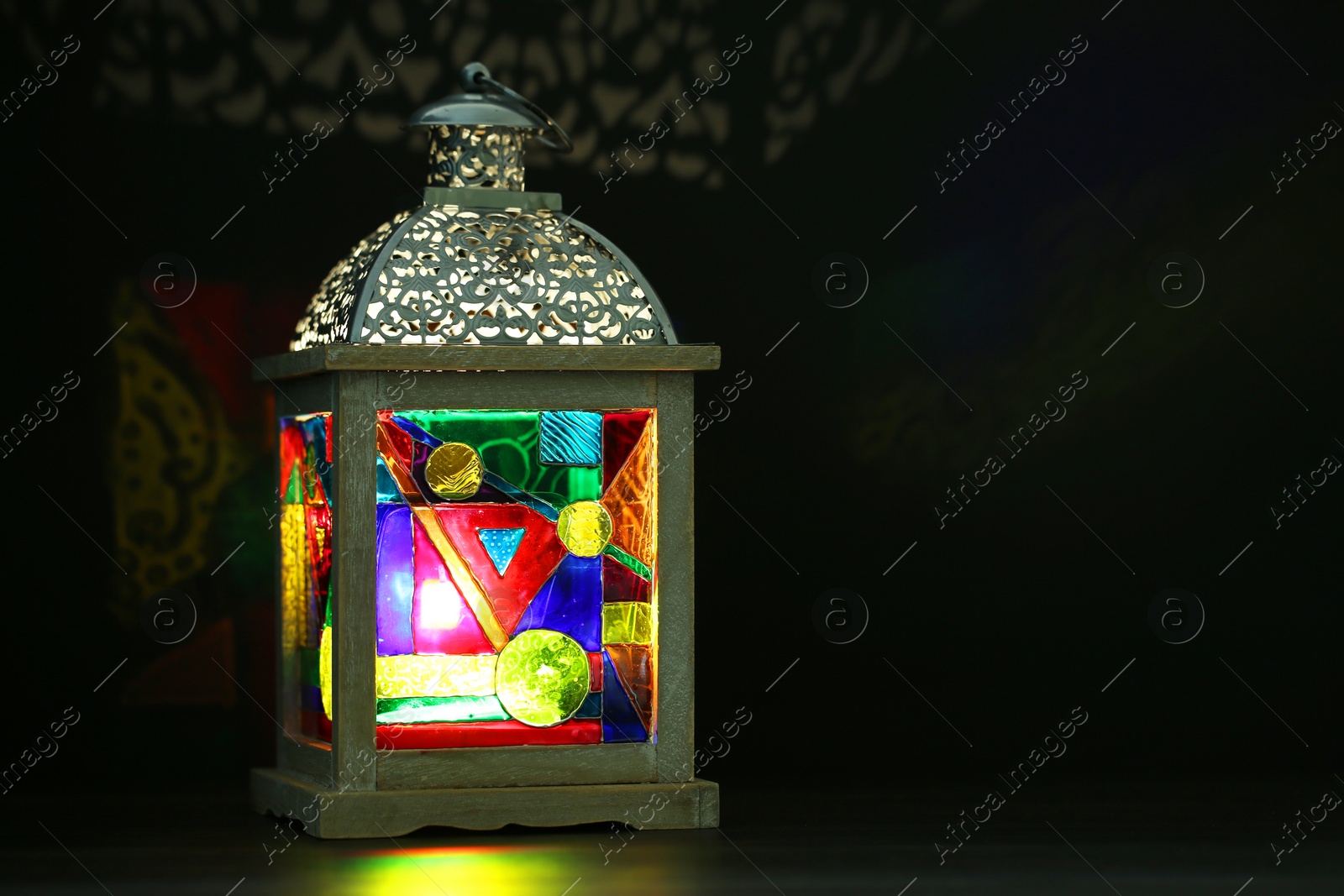 Photo of Decorative Arabic lantern on table against dark background. Space for text