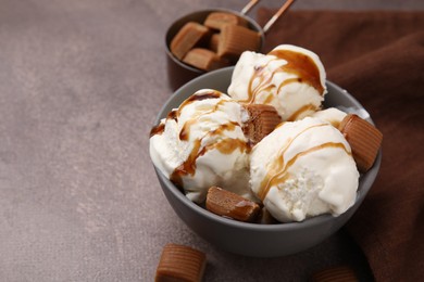 Photo of Scoops of ice cream with caramel sauce and candies on textured table, closeup. Space for text