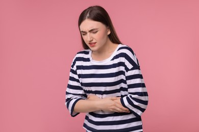 Young woman suffering from stomach pain on pink background