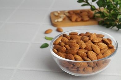 Photo of Bowl of delicious almonds and fresh leaves on white tiled table. Space for text