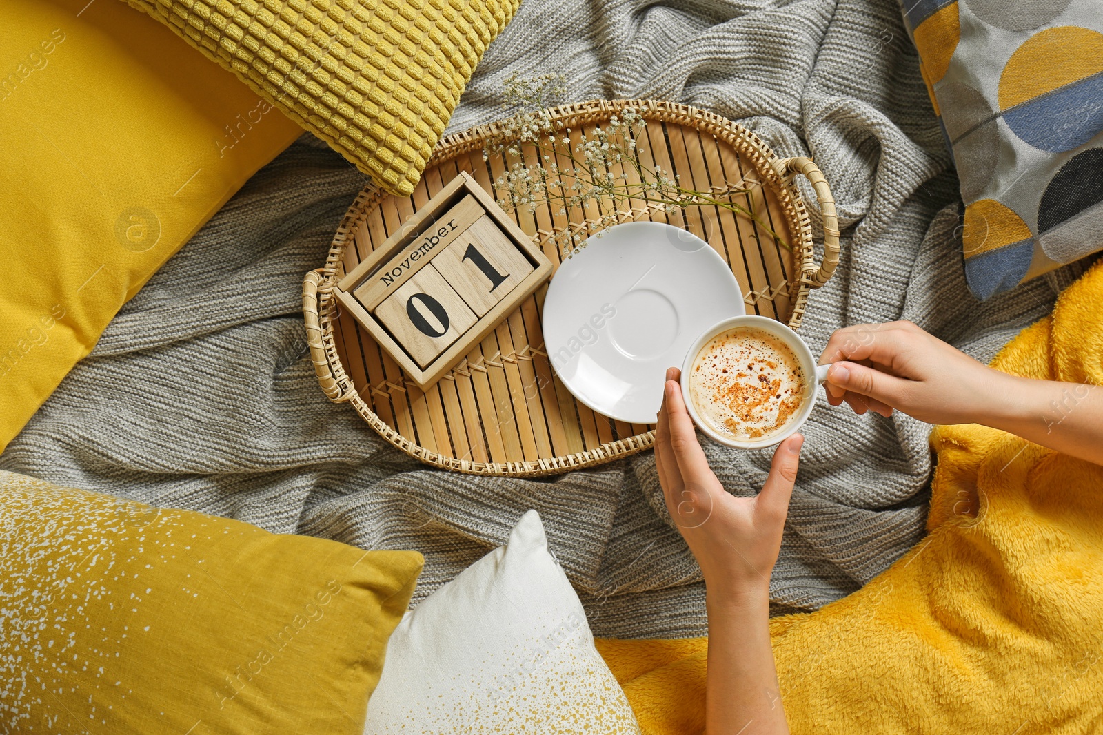 Photo of Woman holding cup of coffee while lying on bed with pillows and warm plaid, top view