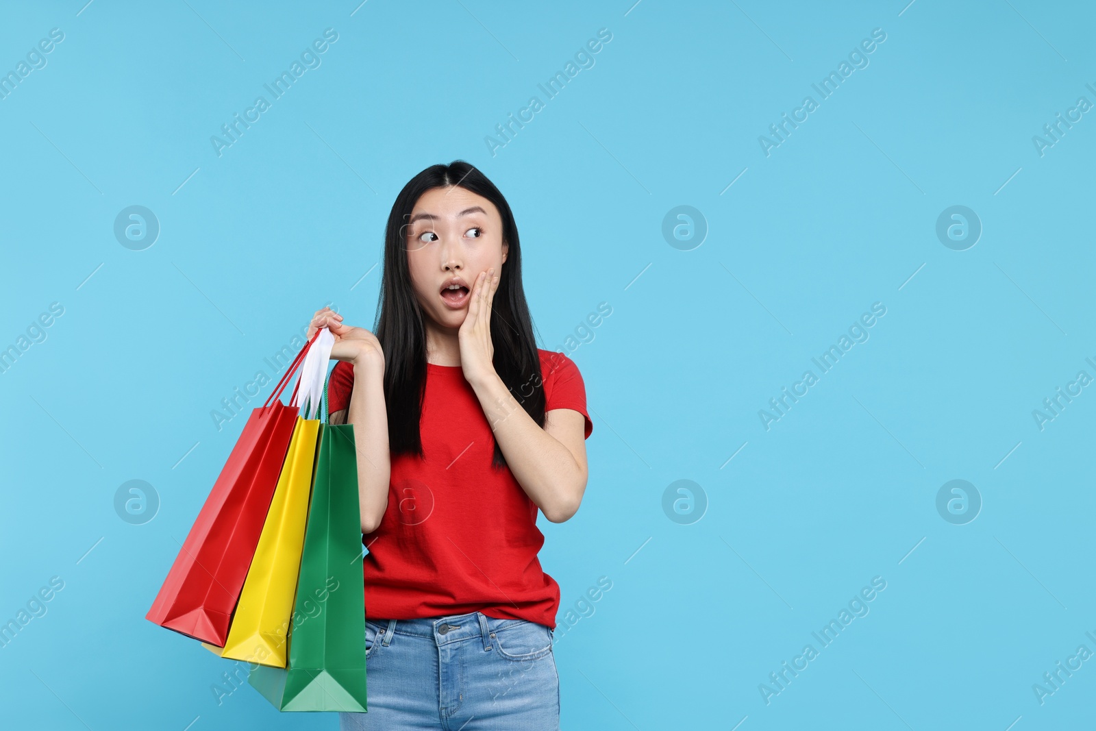 Photo of Surprised woman with shopping bags on light blue background. Space for text
