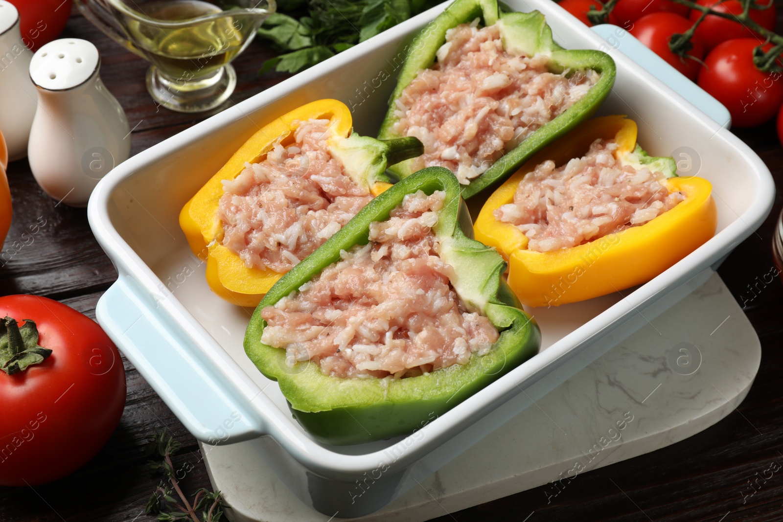 Photo of Raw stuffed peppers in dish and ingredients on wooden table, closeup