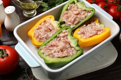 Raw stuffed peppers in dish and ingredients on wooden table, closeup