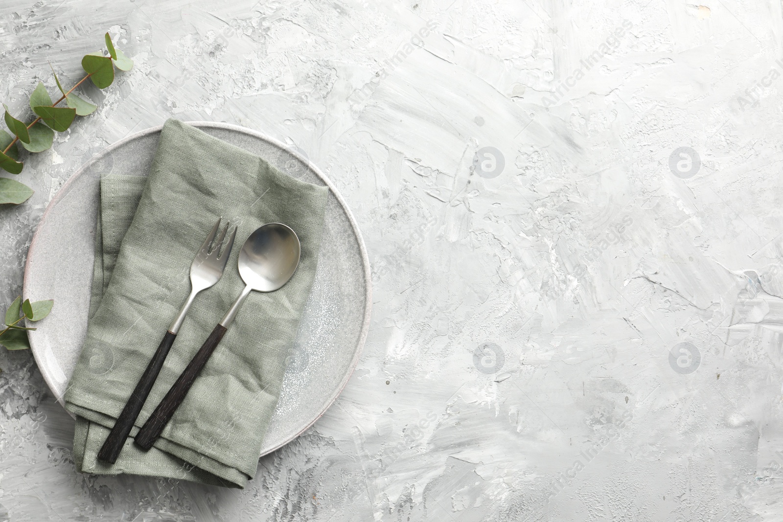 Photo of Stylish setting with cutlery, napkin, eucalyptus branches and plate on grey textured table, flat lay. Space for text