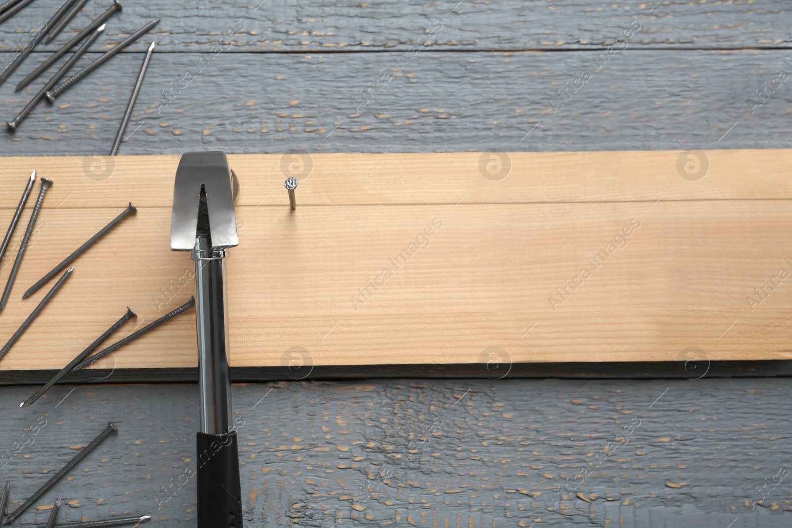 Photo of Hammering nails into plank on grey wooden table, flat lay. Space for text