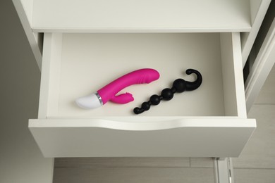 Pink vibrator and anal beads in open drawer of nightstand indoors. Sex toys