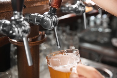 Bartender pouring beer from tap into glass in bar, closeup