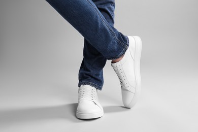 Man wearing stylish white sneakers on grey background, closeup