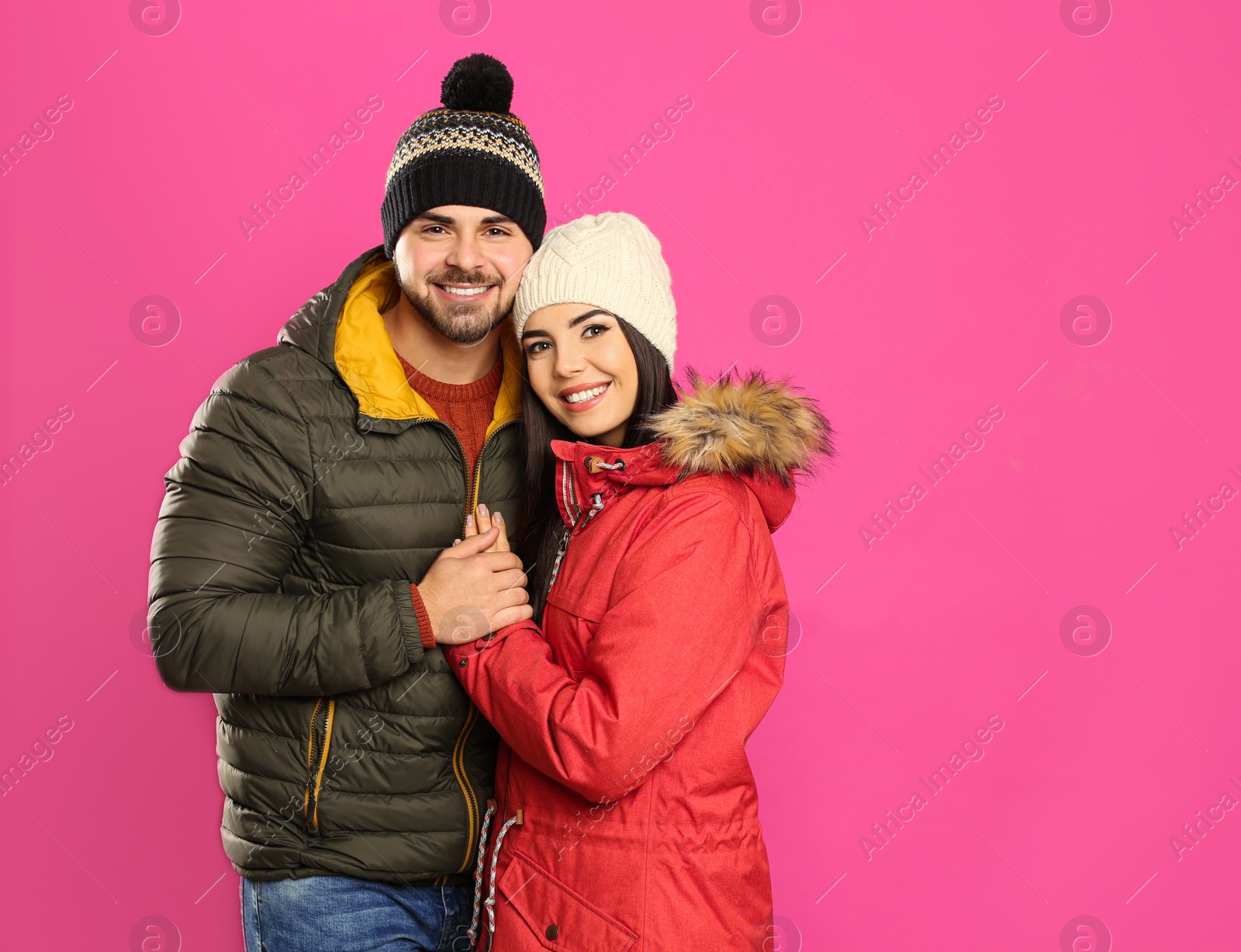 Photo of Happy young couple in warm clothes on pink background, space for text. Winter vacation