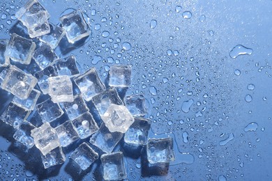 Photo of Melting ice cubes and water drops on blue background, flat lay. Space for text