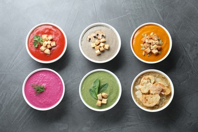 Different tasty cream soups in bowls on dark grey table, flat lay