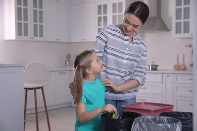 Photo of Young woman and her daughter throwing banana peel into trash bin in kitchen. Separate waste collection