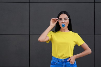 Photo of Beautiful woman blowing gum near dark tiled wall outdoors, space for text