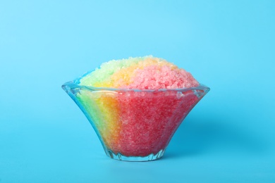 Photo of Rainbow shaving ice in glass dessert bowl on light blue background