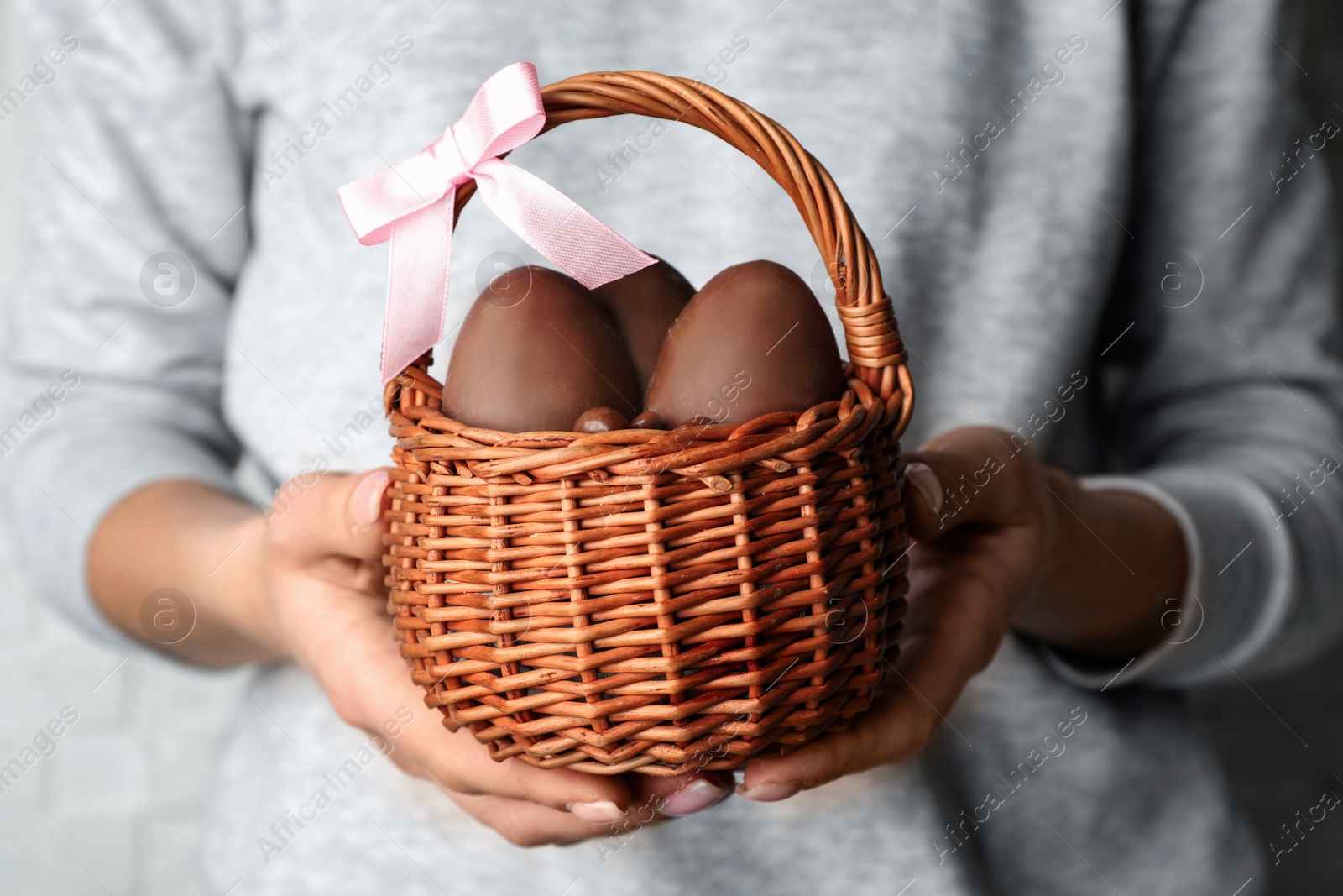 Photo of Woman holding wicker basket with sweet chocolate Easter eggs, closeup