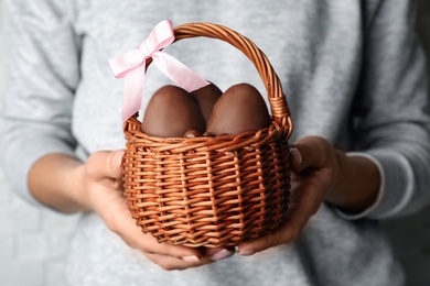 Photo of Woman holding wicker basket with sweet chocolate Easter eggs, closeup