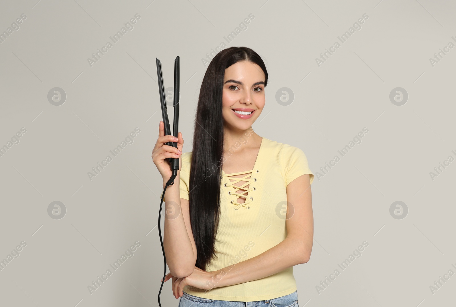 Photo of Beautiful happy woman with hair iron on light grey background