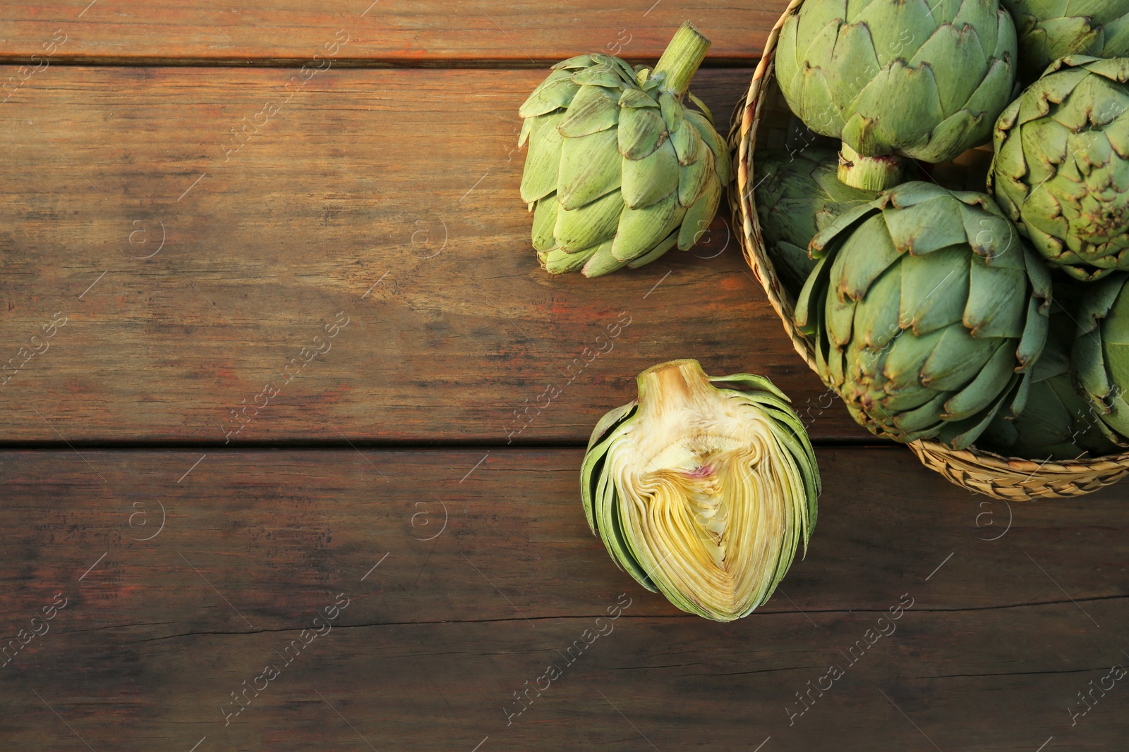 Photo of Whole and cut fresh raw artichokes on wooden table, flat lay. Space for text