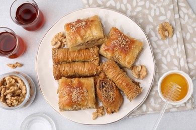 Photo of Eastern sweets. Pieces of tasty baklava, honey and tea on white table, flat lay