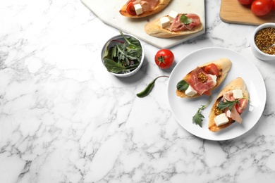 Photo of Bruschettas with prosciutto served on marble table, flat lay