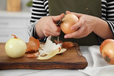 Photo of Woman peeling fresh onion with knife at white marble table indoors, closeup