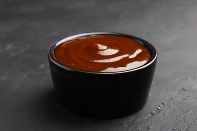 Tasty barbeque sauce in bowl on dark textured table, closeup