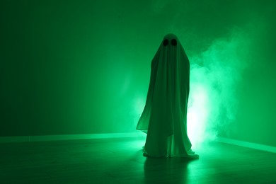 Creepy ghost. Woman covered with sheet in green light, space for text