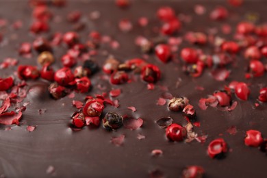 Photo of Delicious chocolate bar with red peppercorns as background, closeup