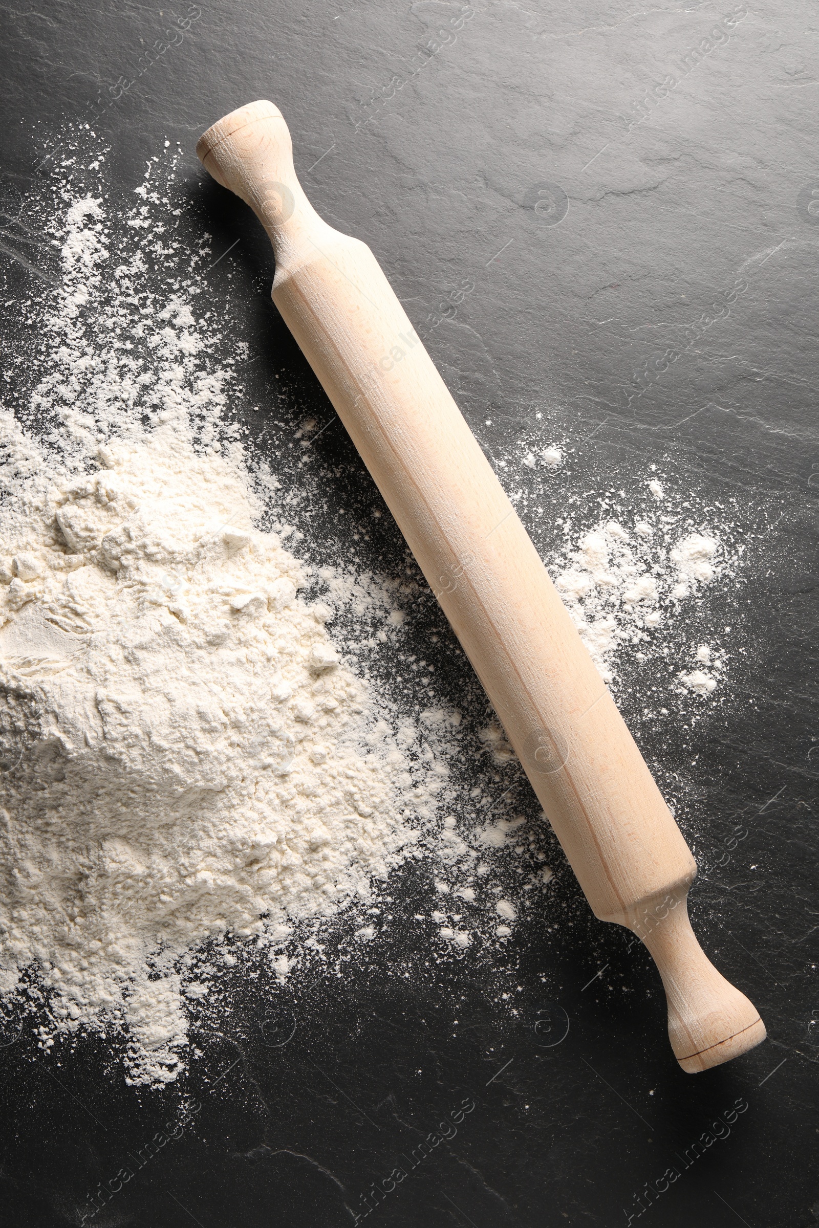 Photo of Pile of flour and rolling pin on black textured table, top view