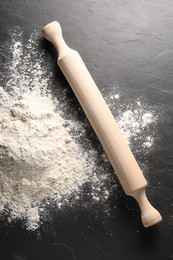 Pile of flour and rolling pin on black textured table, top view