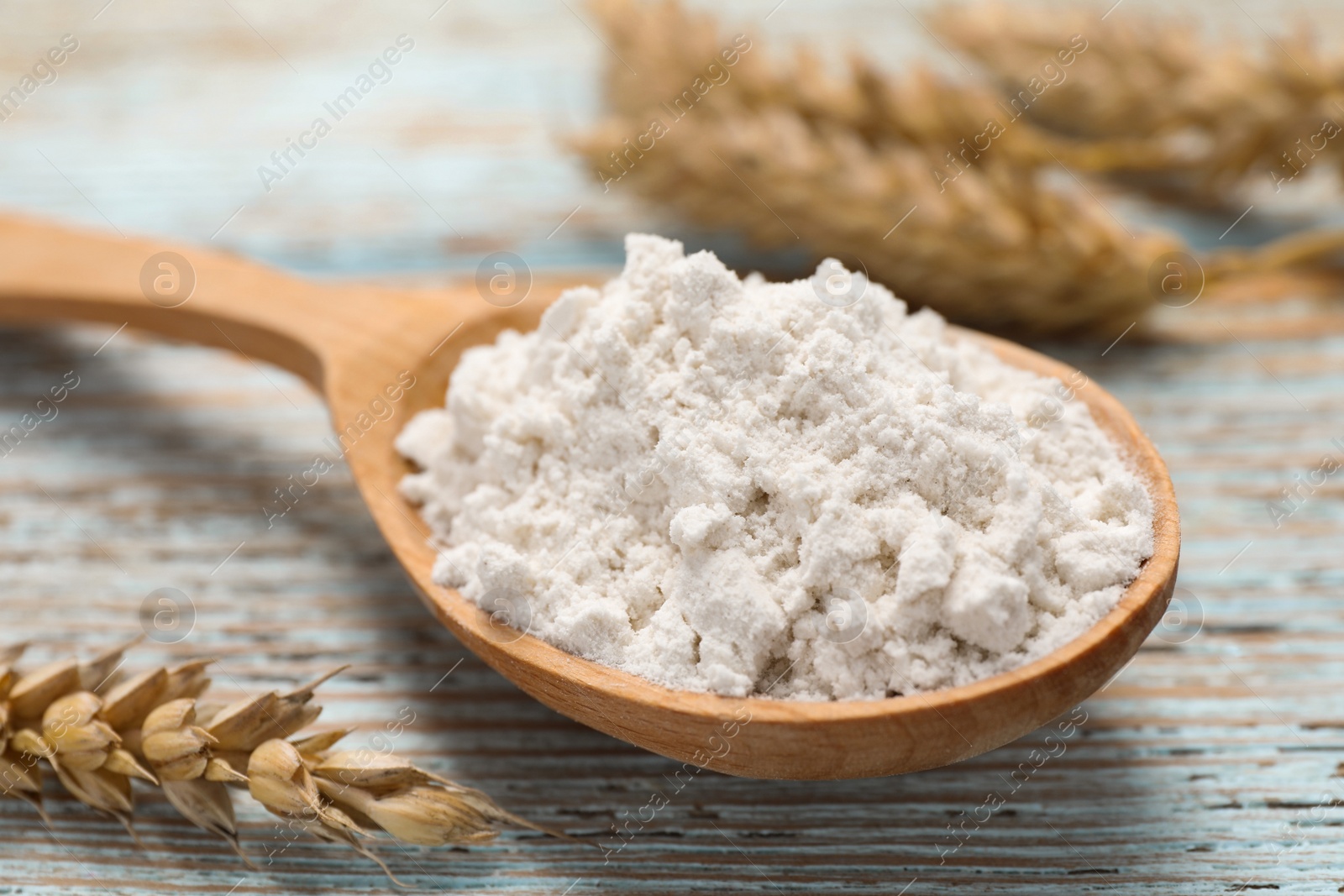 Photo of Spoon of wheat flour on light wooden table, closeup