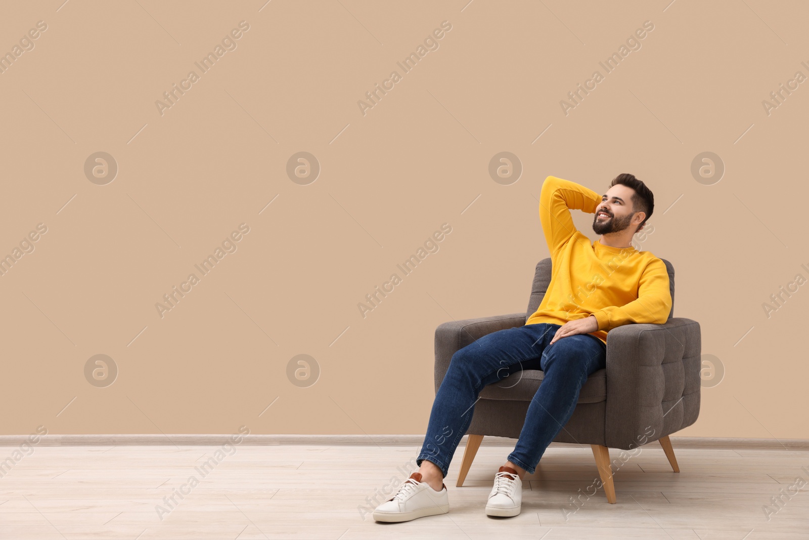 Photo of Handsome man relaxing in armchair near beige wall indoors, space for text