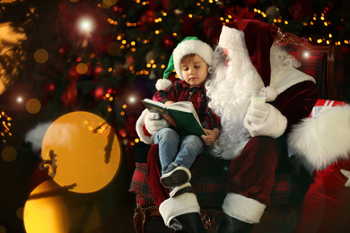 Photo of Santa Claus and little boy with book near Christmas tree indoors