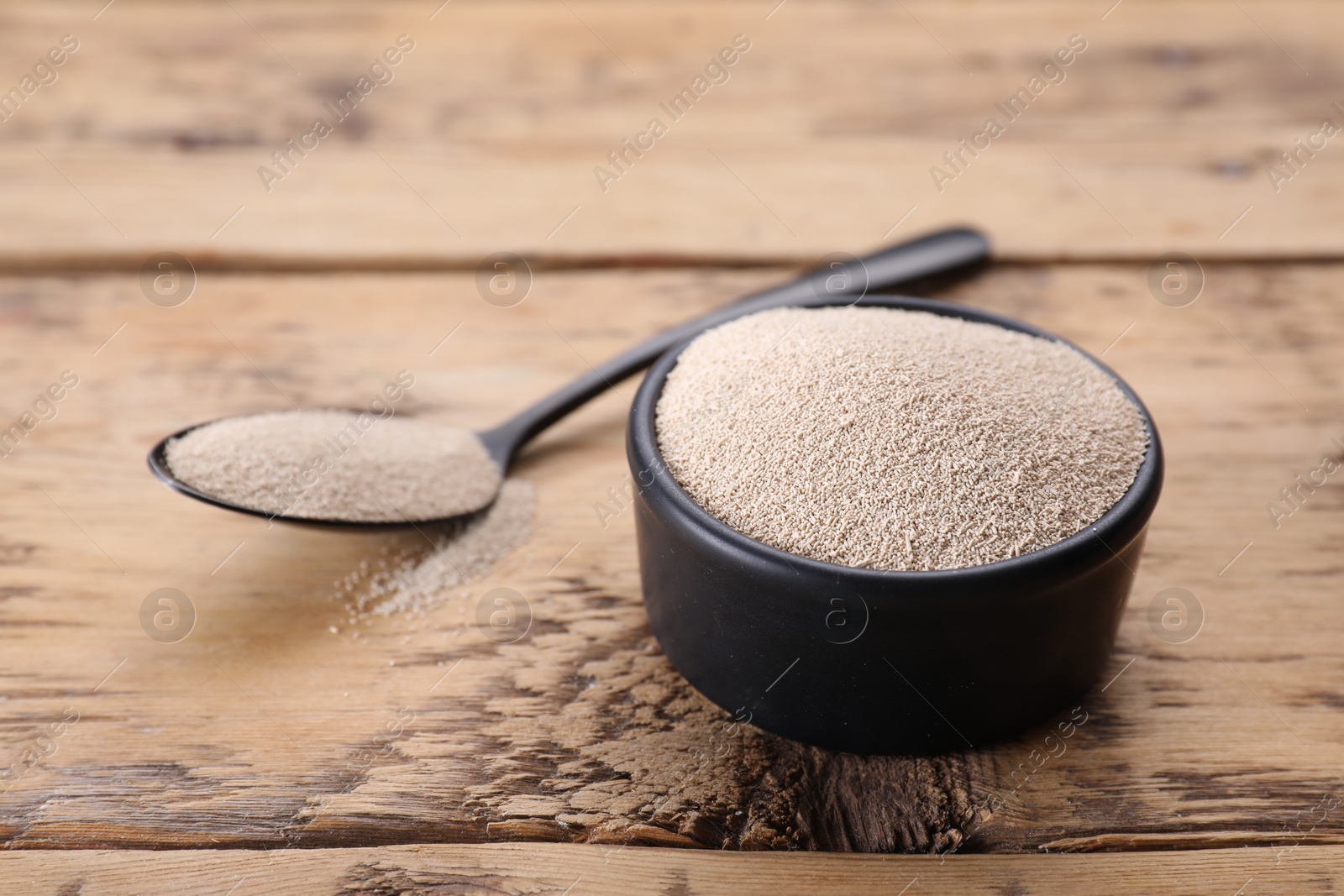 Photo of Bowl and spoon with active dry yeast on wooden table, closeup