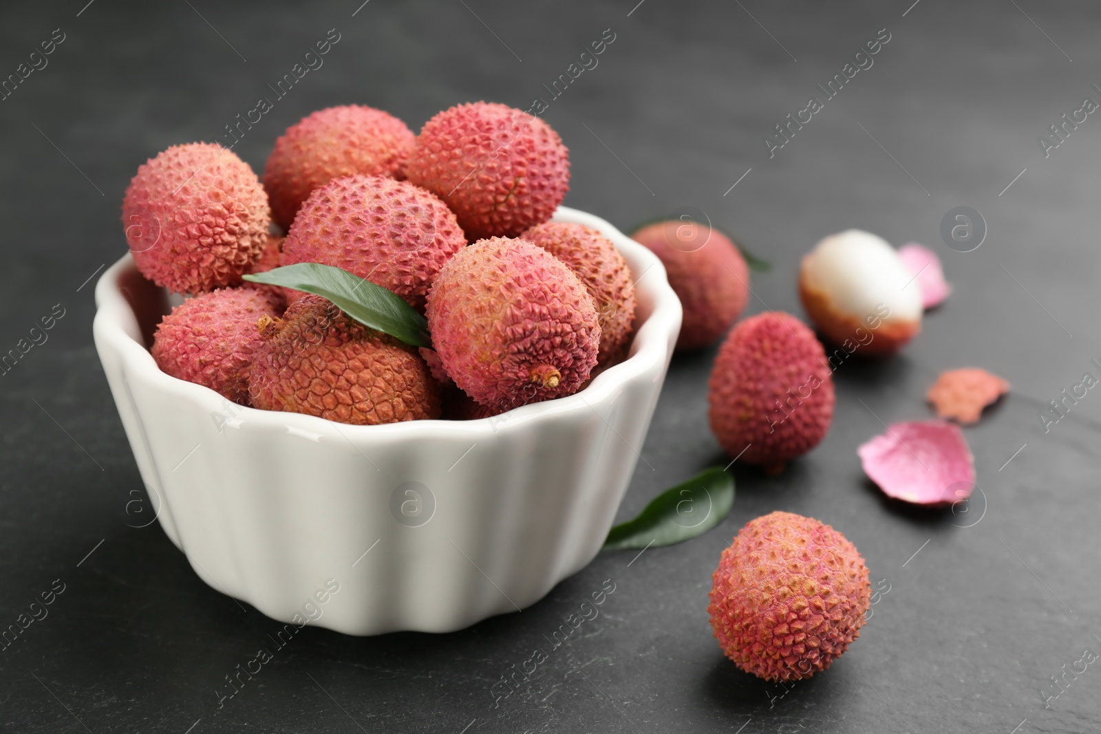 Photo of Fresh ripe lychee fruits in white ceramic bowl on black table