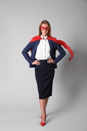 Photo of Confident businesswoman wearing superhero cape and mask on light grey background