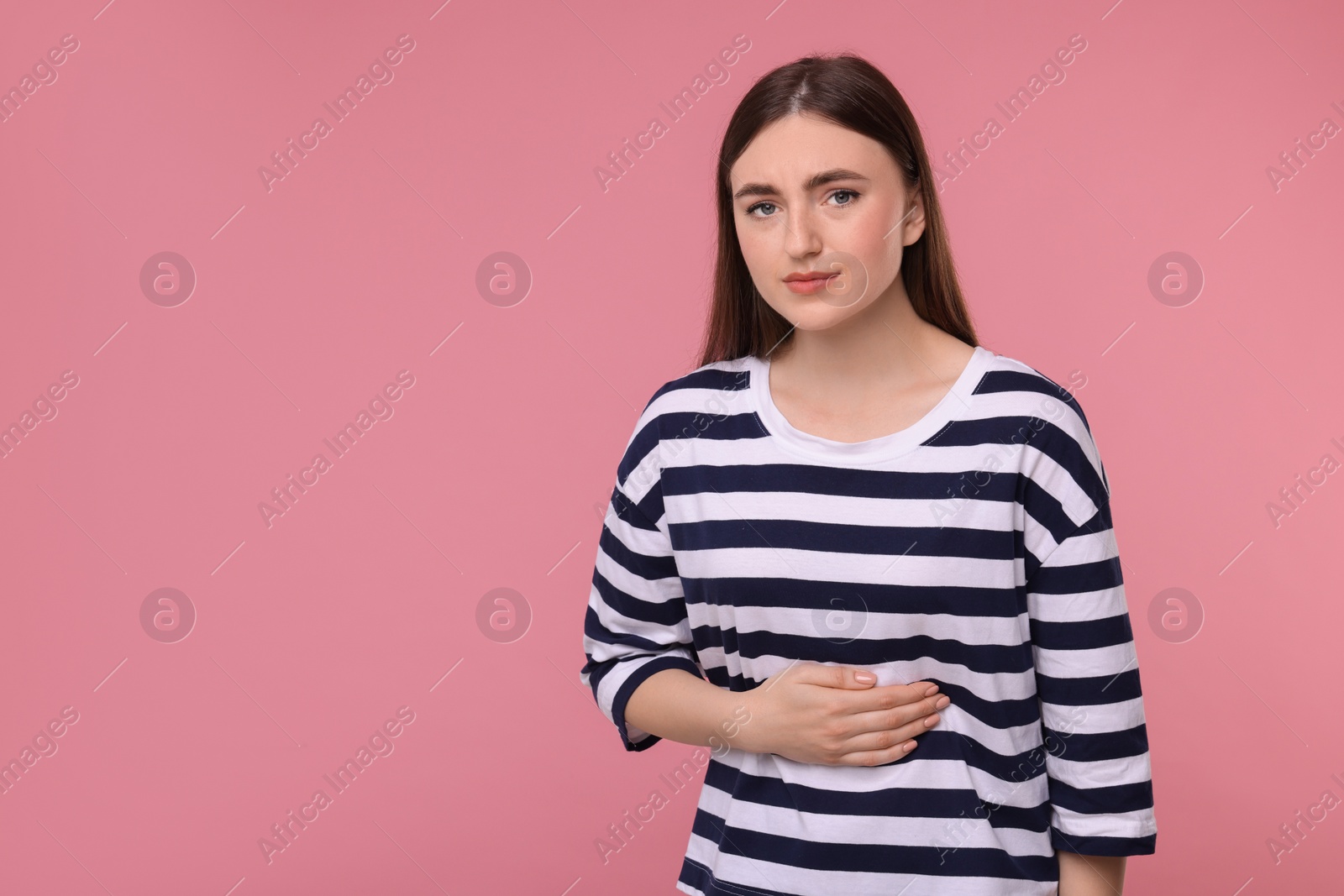 Photo of Young woman suffering from stomach pain on pink background. Space for text