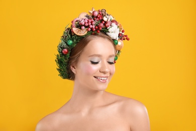 Beautiful young woman wearing Christmas wreath on yellow background