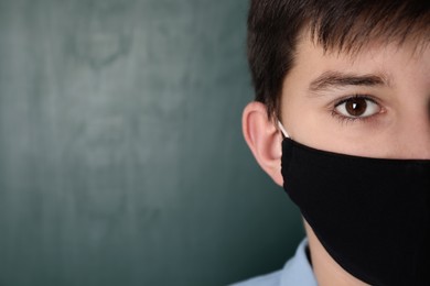 Closeup view of boy wearing protective mask near chalkboard, space for text. Child safety